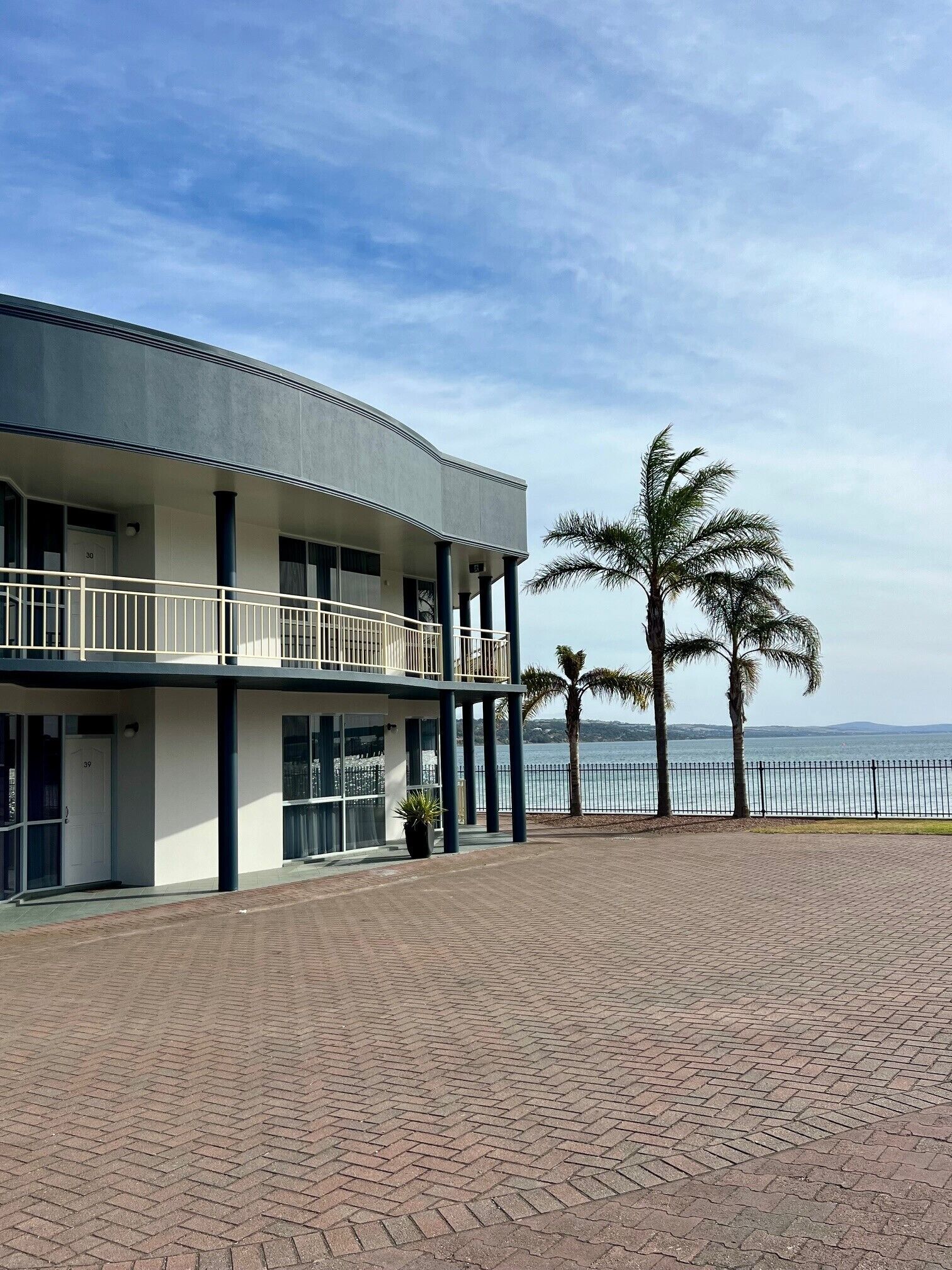 A building with a balcony, a paved walkway, and a view of the sea.