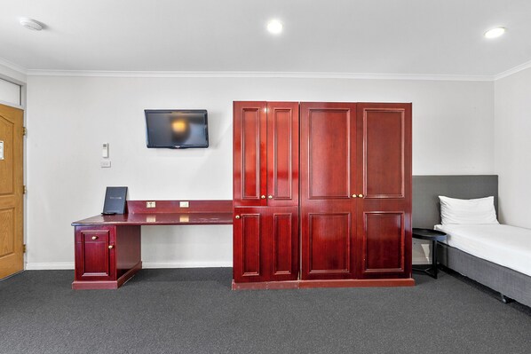 A room with a desk, wardrobe, bed, and a TV mounted on the wall.