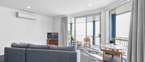 A modern hotel room with a grey sofa, a small round table, and a TV.
