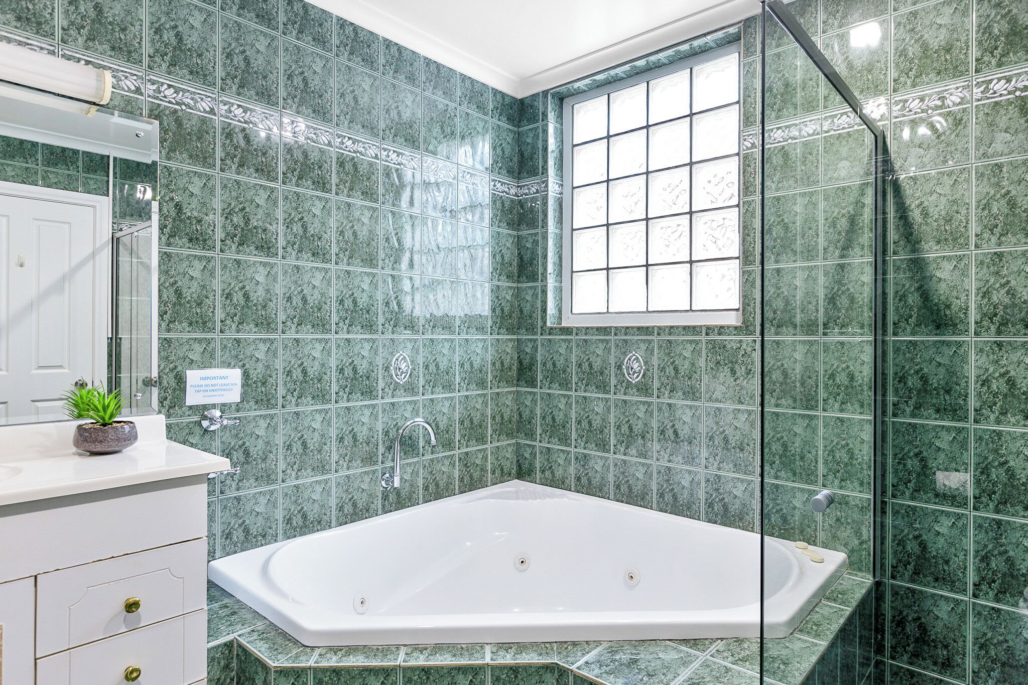 A modern bathroom with a large bathtub, green marble tiles, a glass shower enclosure, and a window with decorative glass panes.