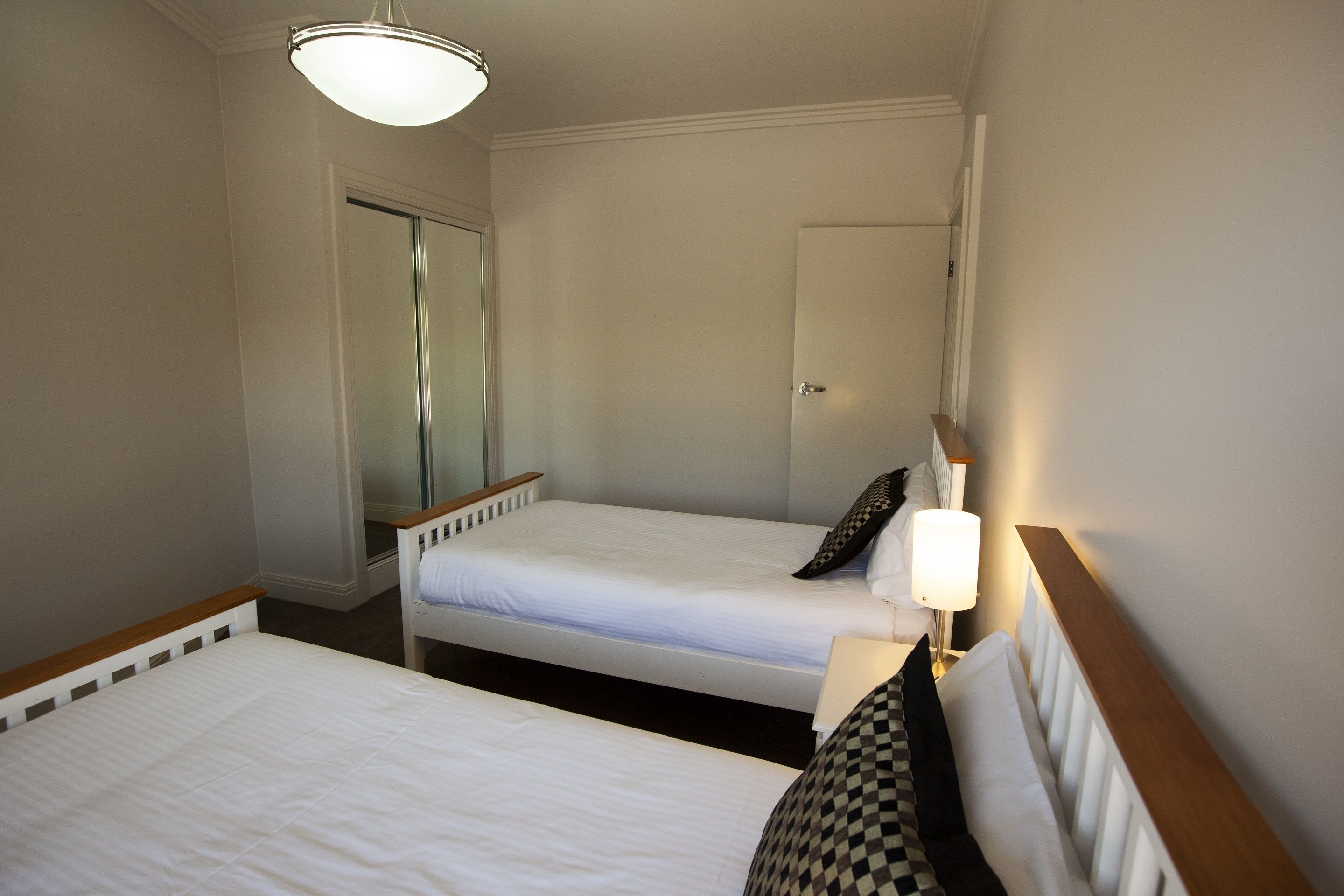 A hotel room with two single beds, a bedside table with a lamp, a door, and a mirror.