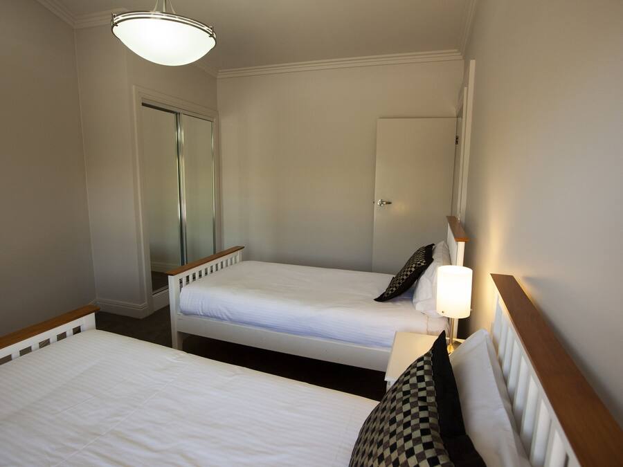 A hotel room with two single beds, a bedside table with a lamp, a door, and a mirror.
