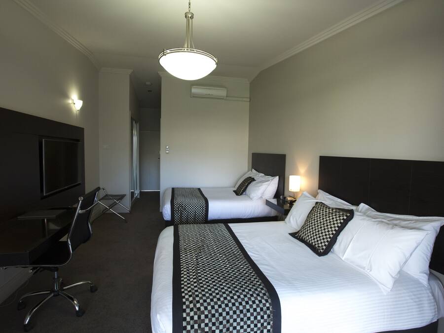 A hotel room with two beds, a desk, a chair, a TV, and a ceiling light.