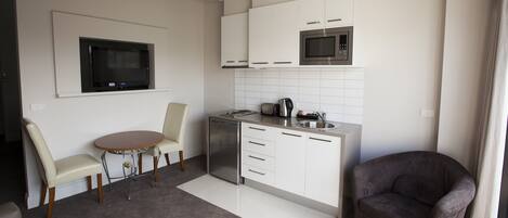 Une cuisine compacte avec des meubles blancs, un four à micro-ondes et un petit coin repas comprenant une table et deux chaises.