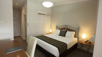 Habitación de hotel ordenada con cama, mesitas de noche, escritorio y una silla.