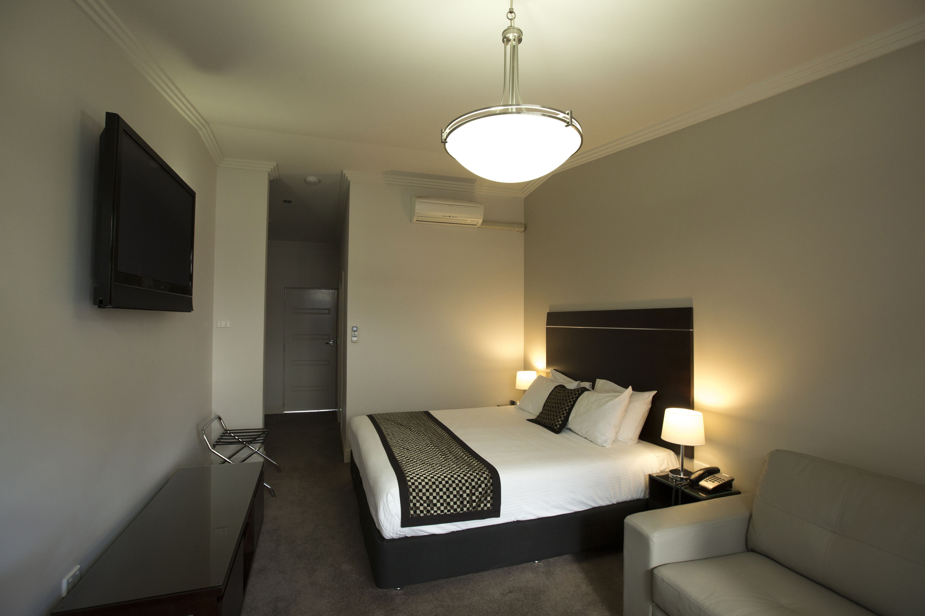 A hotel room with a bed, bedside table, lamp, and a TV mounted on the wall.