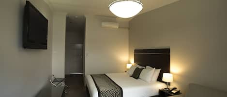 Una habitación de hotel con cama, mesita de noche, lámpara y televisor montado en la pared.