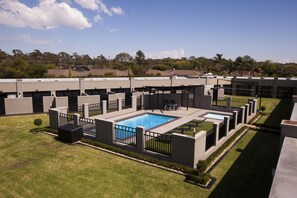 A modern building with a swimming pool, surrounded by well-maintained lawns and a clear sky.