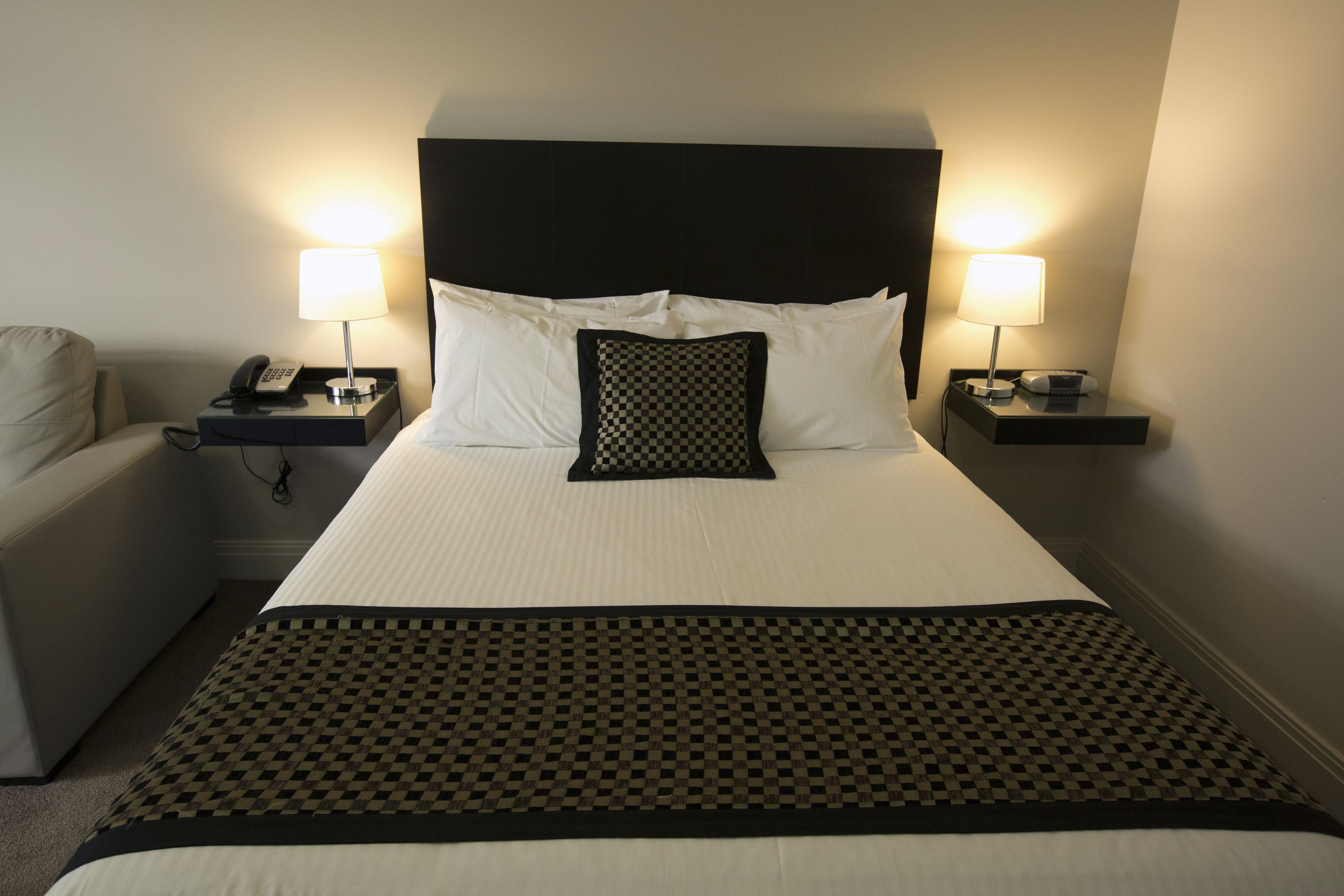 A hotel room with a large bed, two bedside tables with lamps, a telephone, and a chair.
