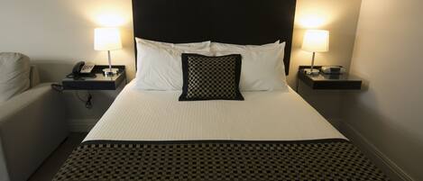 A hotel room with a large bed, two bedside tables with lamps, a telephone, and a chair.