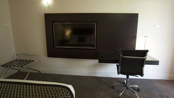 A modern hotel room with a flat-screen TV mounted on the wall, a desk with a chair, and a patterned bedspread.