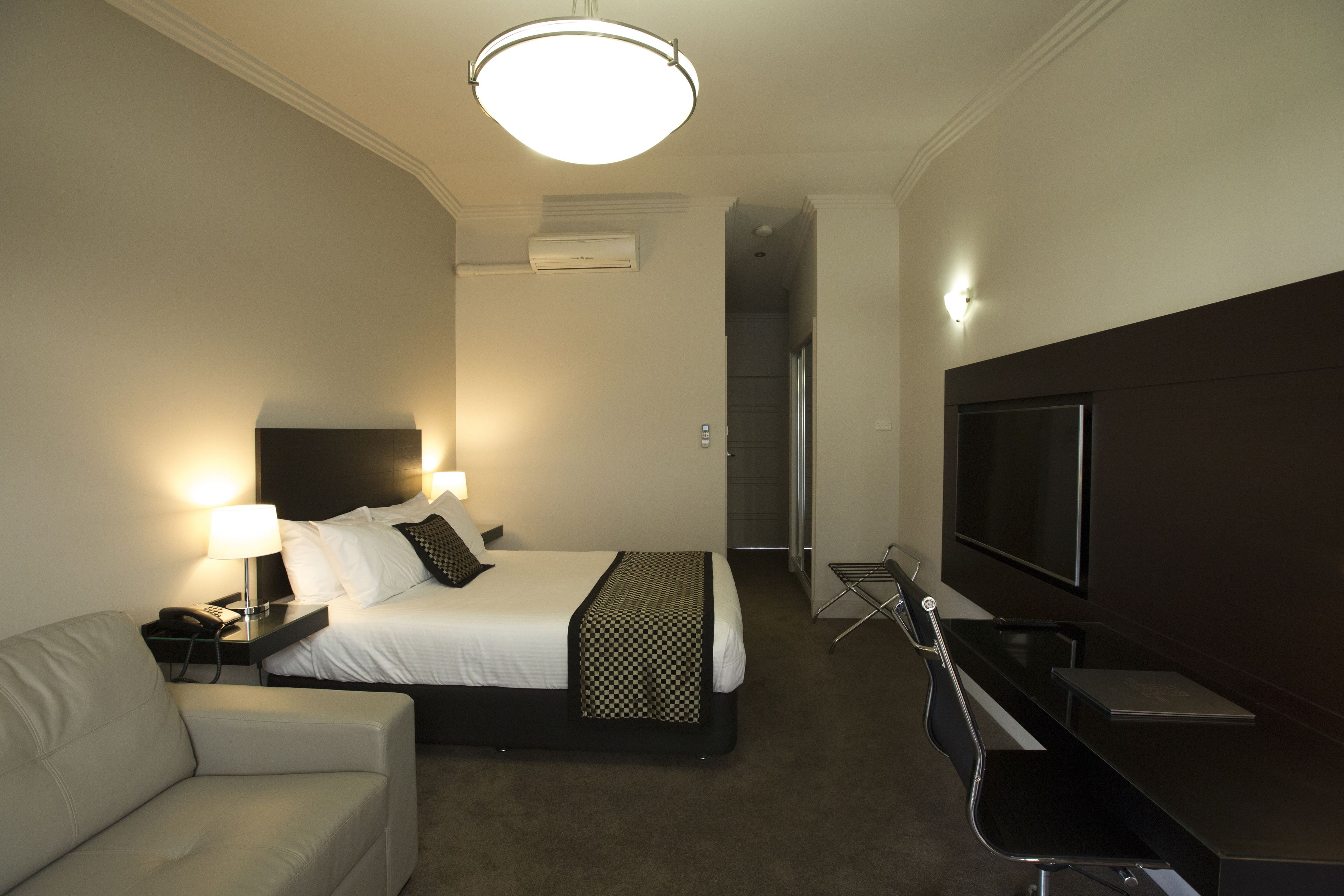 Una habitación de hotel con cama, escritorio, silla, televisor y lámpara.