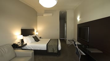Una habitación de hotel con cama, escritorio, silla, televisor y lámpara.