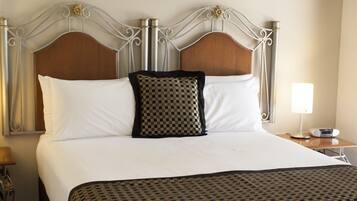 A neatly made bed with a patterned bedspread, a wooden headboard, and a bedside table with a lamp and a phone.