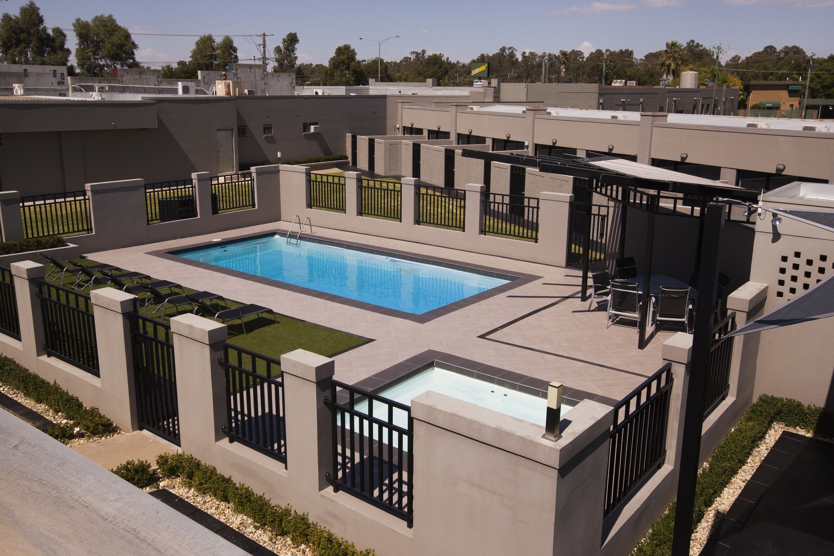 Un espace piscine aménagé sur le toit, avec une piscine rectangulaire, entourée d’un petit muret et de rampes noires.