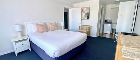 A hotel room with a large bed, a bedside table with a lamp, a chair, and a desk with a computer.