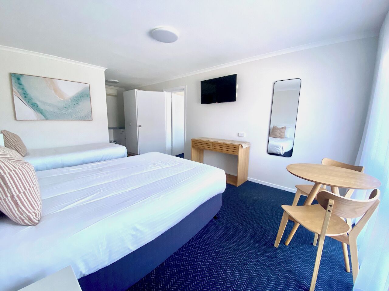 A hotel room with a large bed, a desk, a chair, a TV, and a mirror.