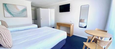 A hotel room with a large bed, a desk, a chair, a TV, and a mirror.