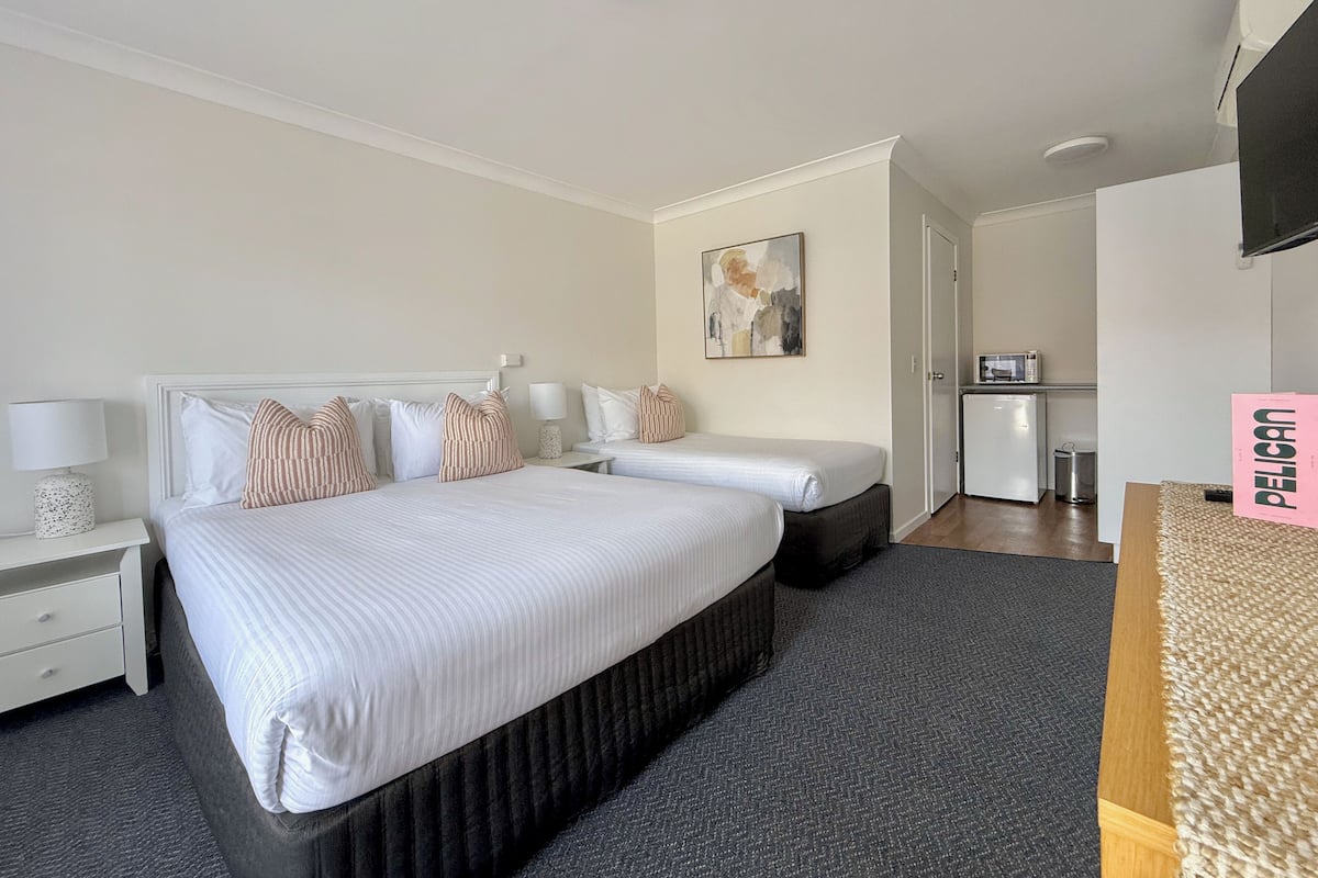 Quarto de hotel com uma cama grande, uma escrivaninha, uma cadeira, uma kitchenette pequena e uma televisão.