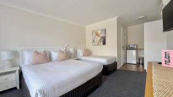 A hotel room with a large bed, a desk, a chair, a small kitchenette, and a TV.