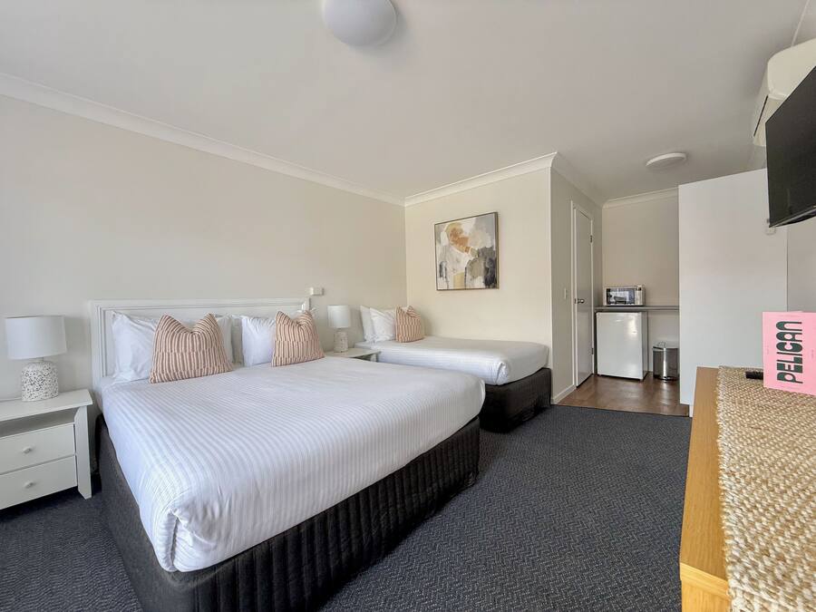A hotel room with a large bed, a desk, a chair, a small kitchenette, and a TV.