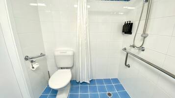 A bathroom with a white toilet, blue-tiled floor, and a shower area with a white curtain.