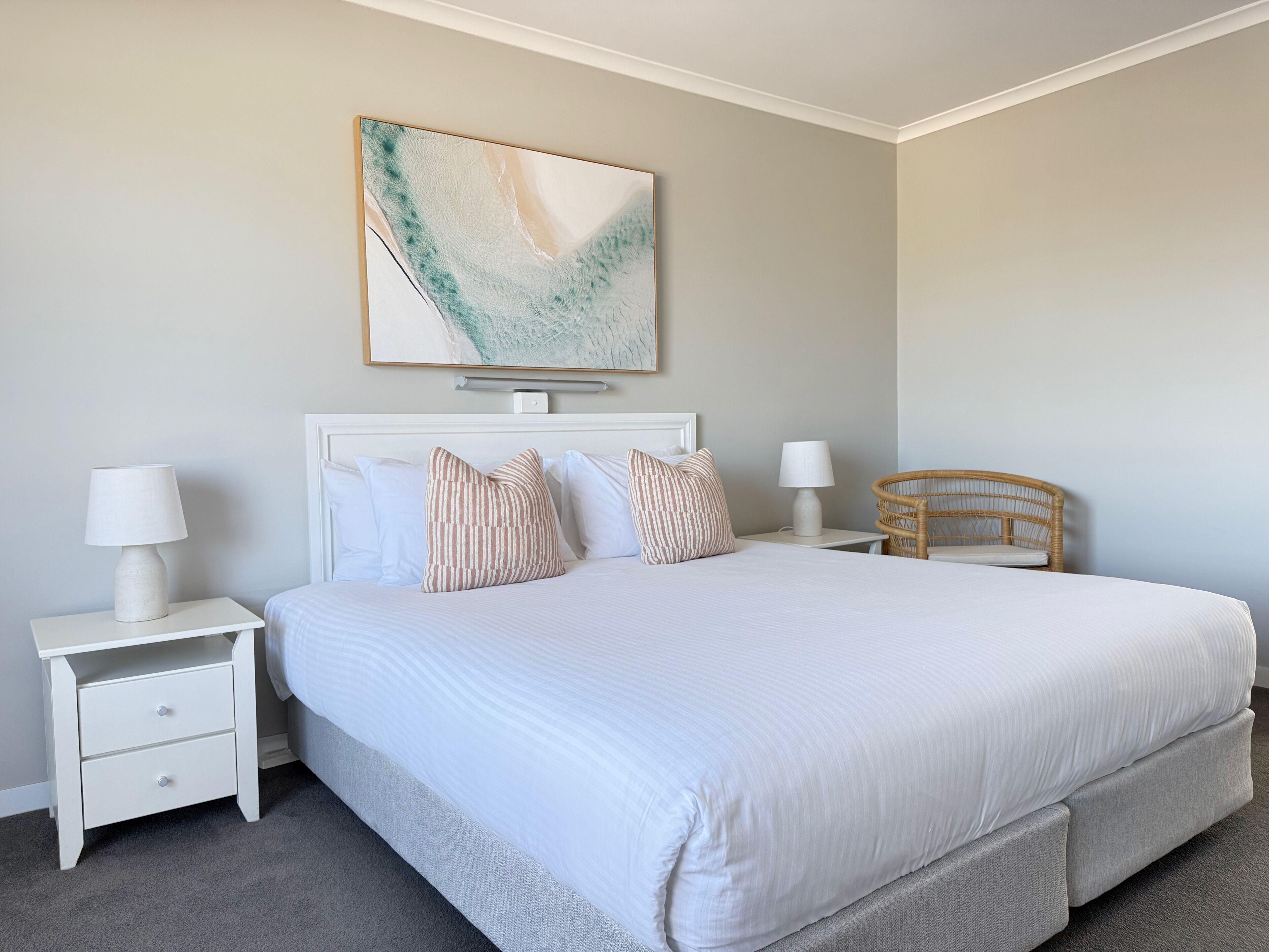 Une chambre à coucher bien aménagée, avec un grand lit, deux tables de chevet, une chaise et une œuvre d’art accrochée au mur.