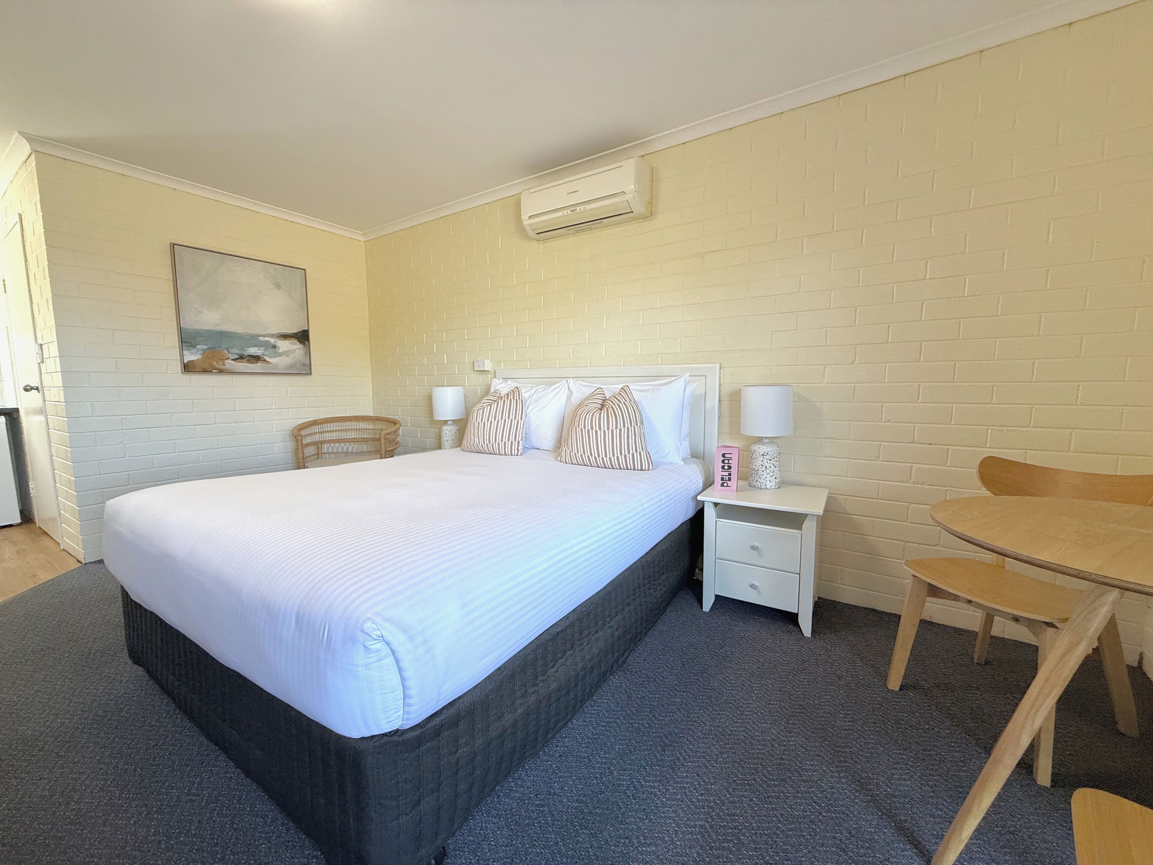 A hotel room with a large bed, a bedside table with a lamp, a chair, and a small table.