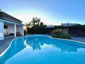 A swimming pool with a covered patio area, lounge chairs, and umbrellas.