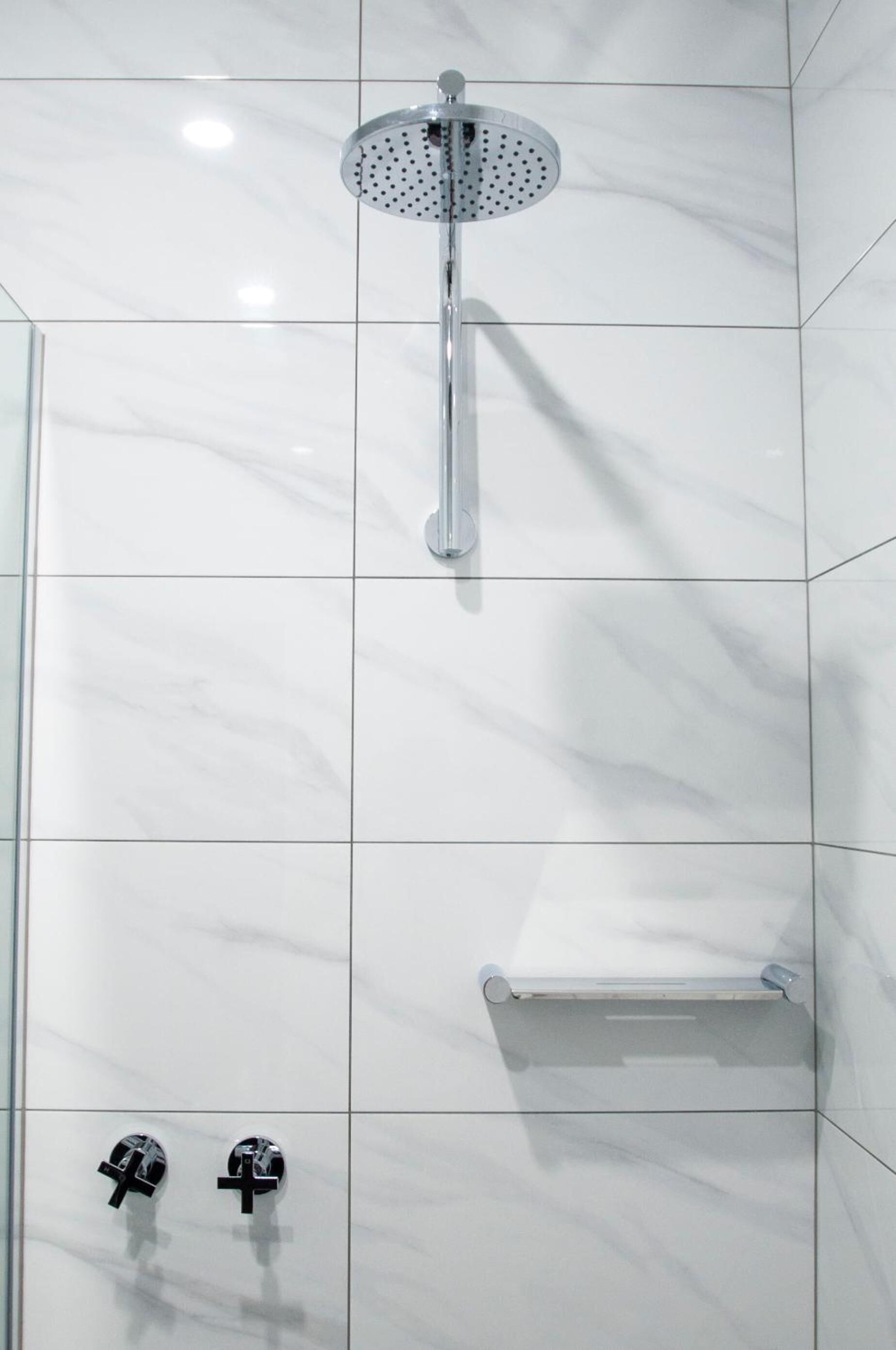 A modern bathroom with a glass shower enclosure, a handheld showerhead, and two wall-mounted faucets.
