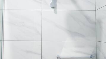 A modern bathroom with a glass shower enclosure, a handheld showerhead, and two wall-mounted faucets.