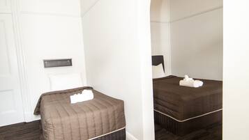 A bedroom with two beds, dark wooden flooring, white walls, and an arched doorway.
