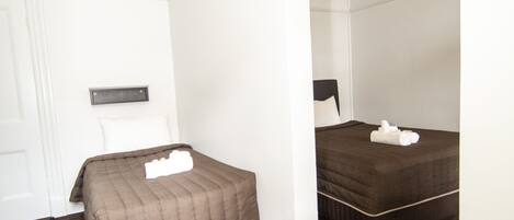 A bedroom with two beds, dark wooden flooring, white walls, and an arched doorway.