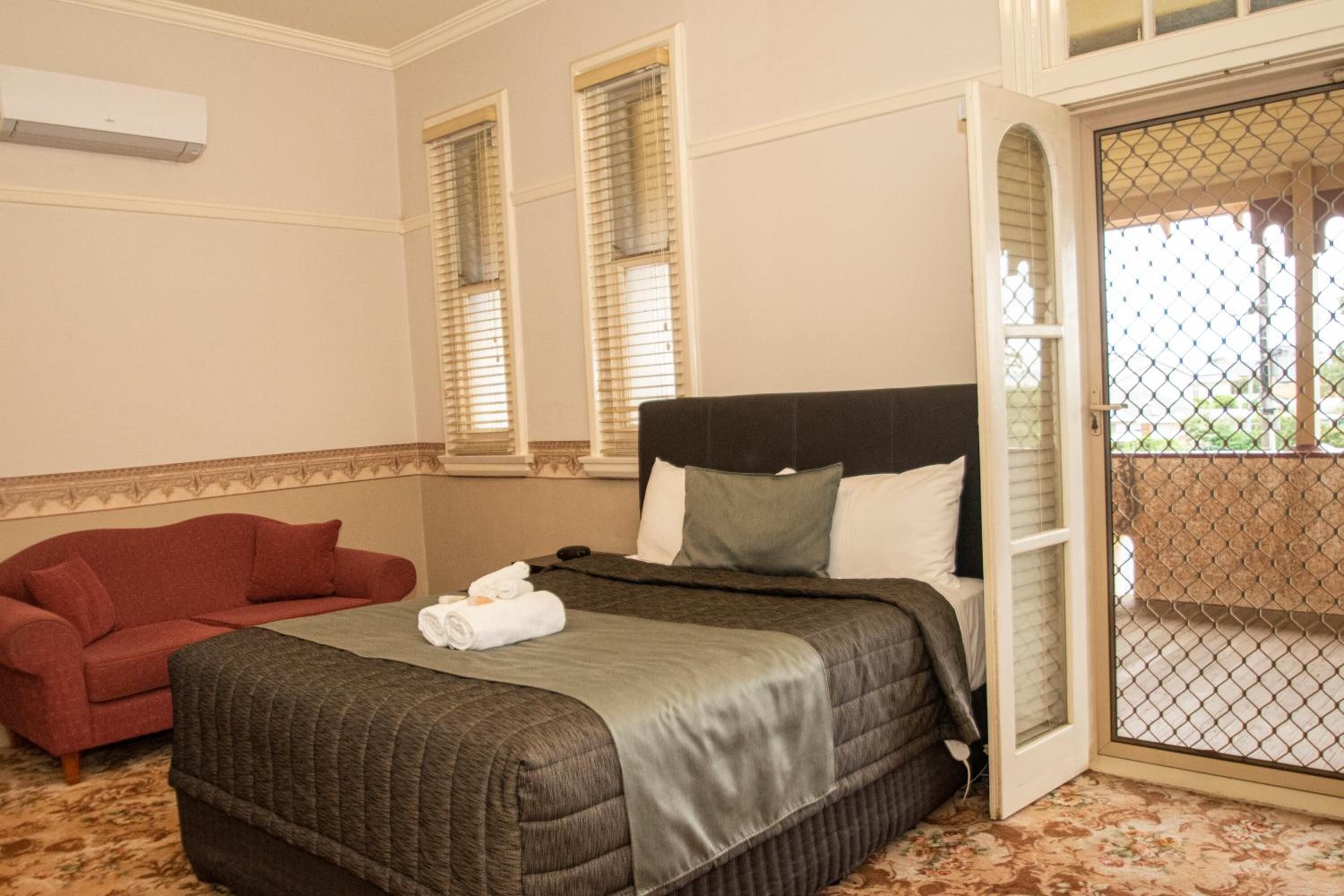 A hotel room with a large bed, a red sofa, and a balcony with a mesh screen.