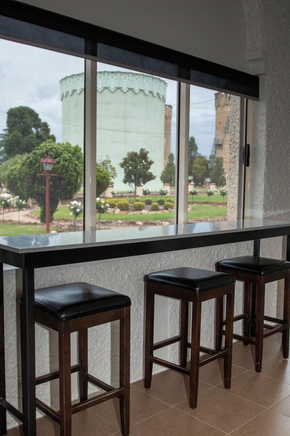 Angolo bar con due sgabelli e vista su un edificio e vegetazione.