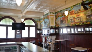 A bar area with a counter, bar stools, and a mural depicting a street scene. - Hydro Hotel (Leeton)