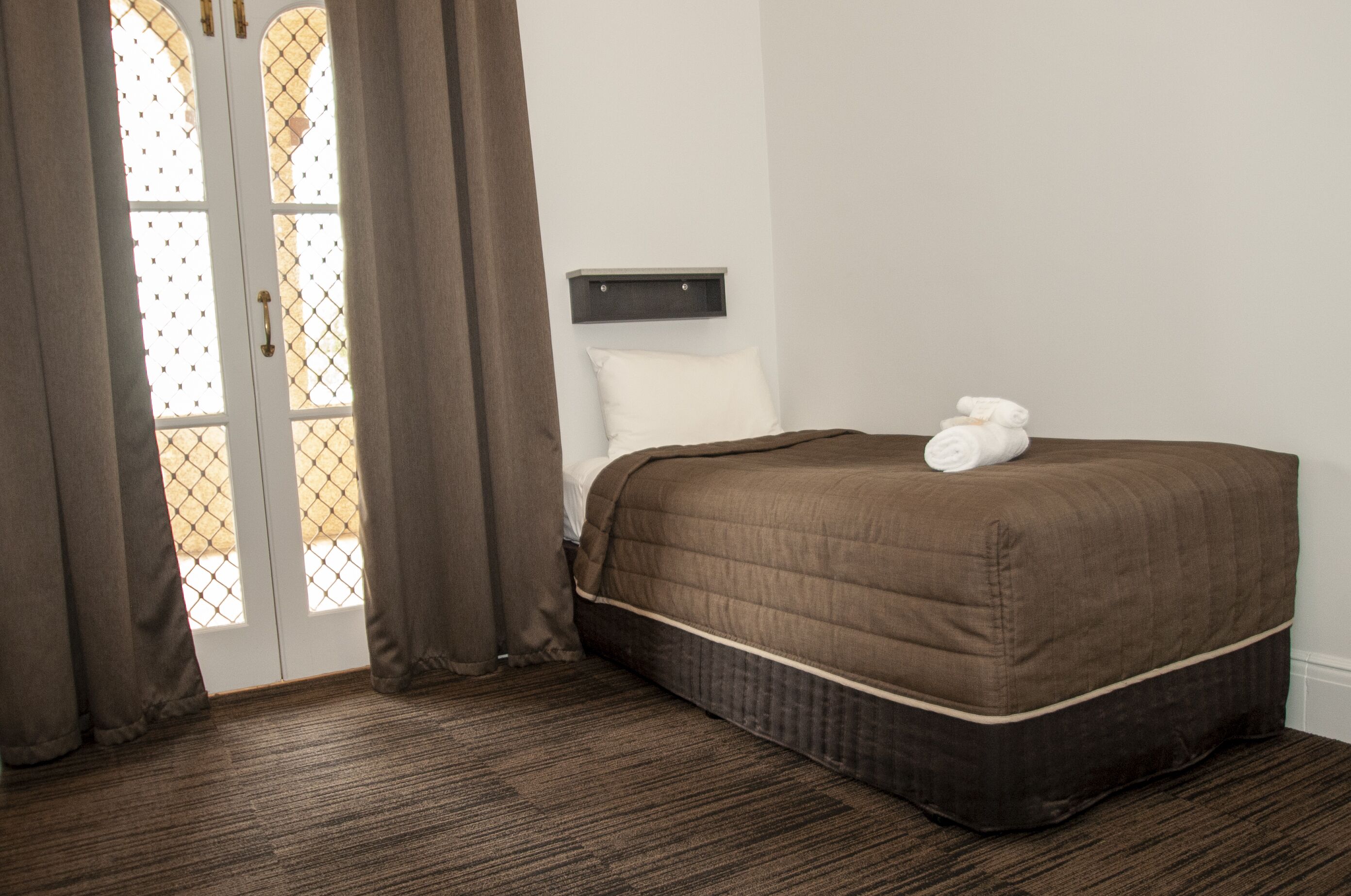 Quarto de hotel com uma cama grande, uma mesa de cabeceira, uma janela com cortinas e vista para o exterior.