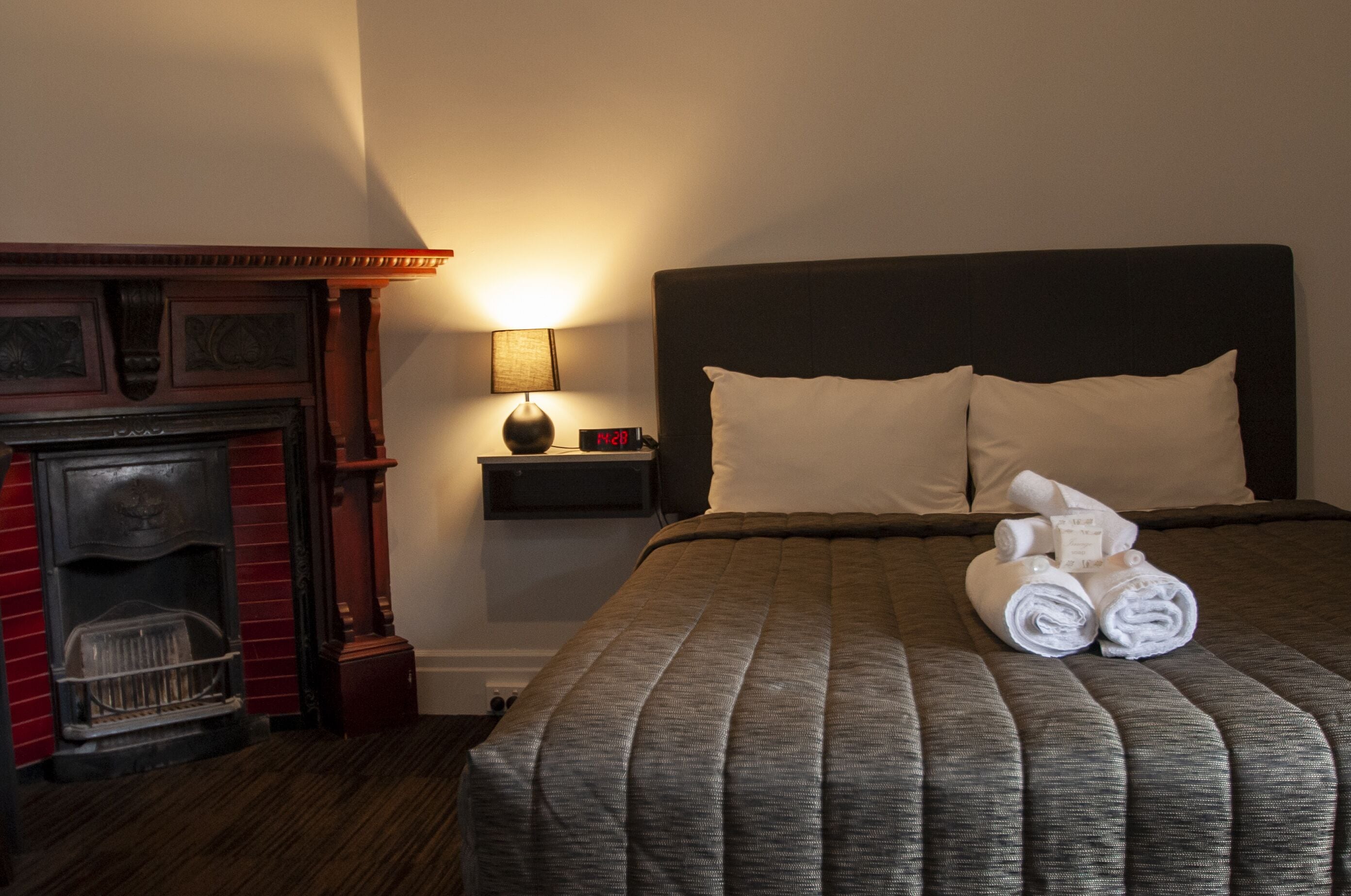 Una habitación de hotel con cama, mesita de noche, lámpara y chimenea.
