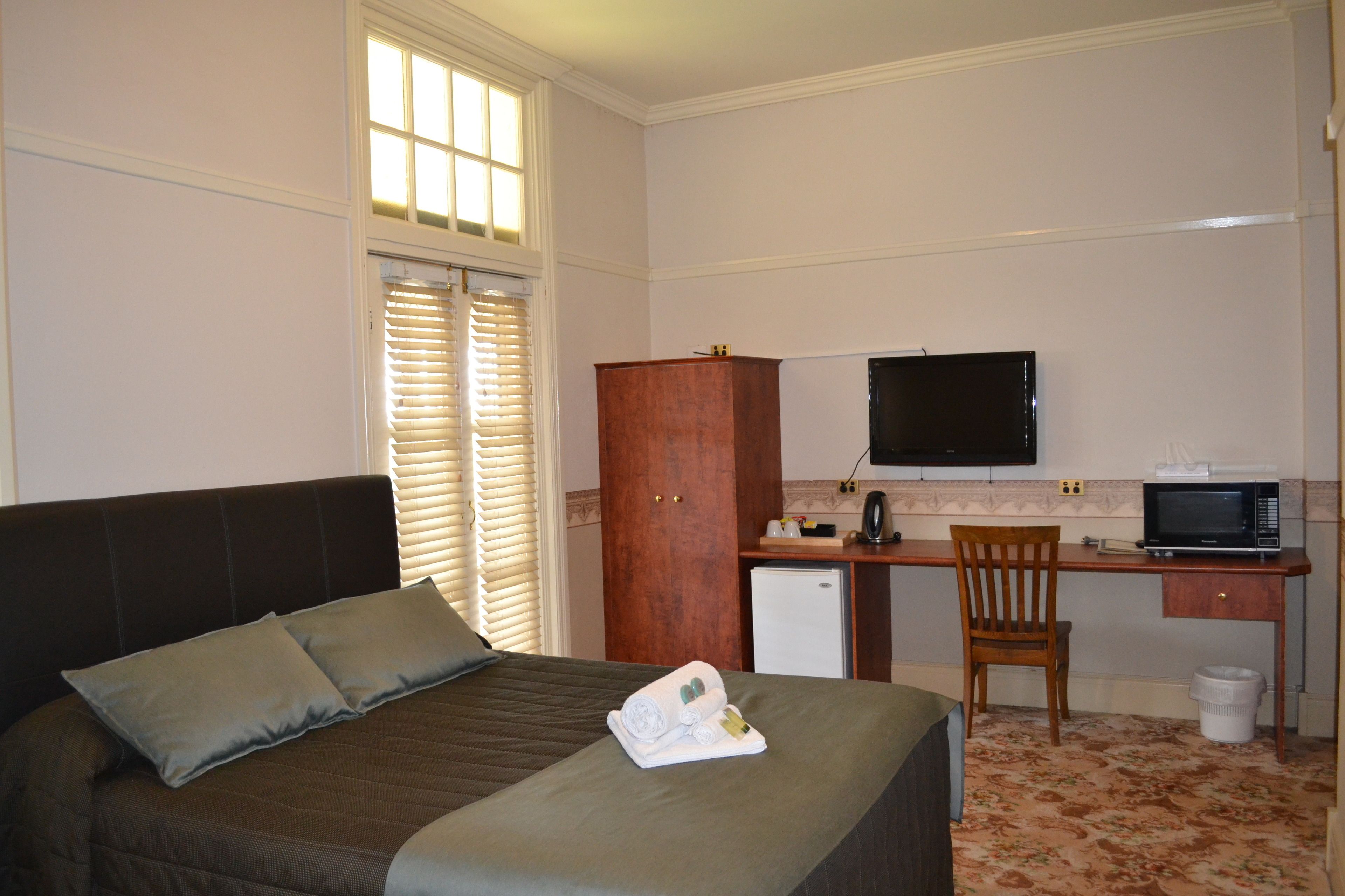 A hotel room with a bed, a desk with a television, a microwave, and a small refrigerator.