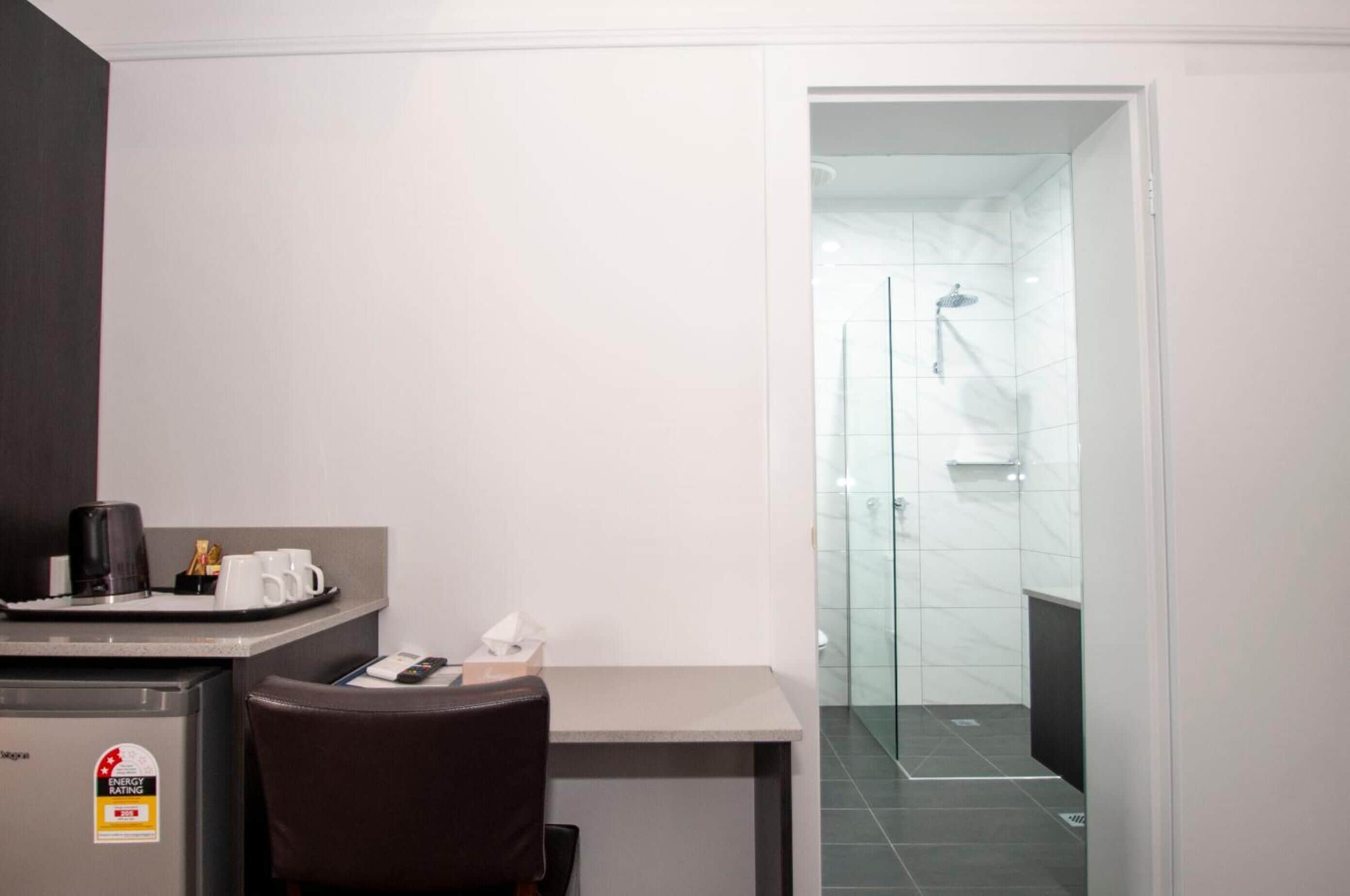 Habitación de hotel compacta con kitchenette, un escritorio pequeño y zona de ducha.