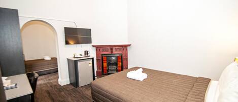 Une chambre d’hôtel équipée d’un lit, d’un bureau, d’une télévision, d’une cheminée et d’une porte en arc de cercle.