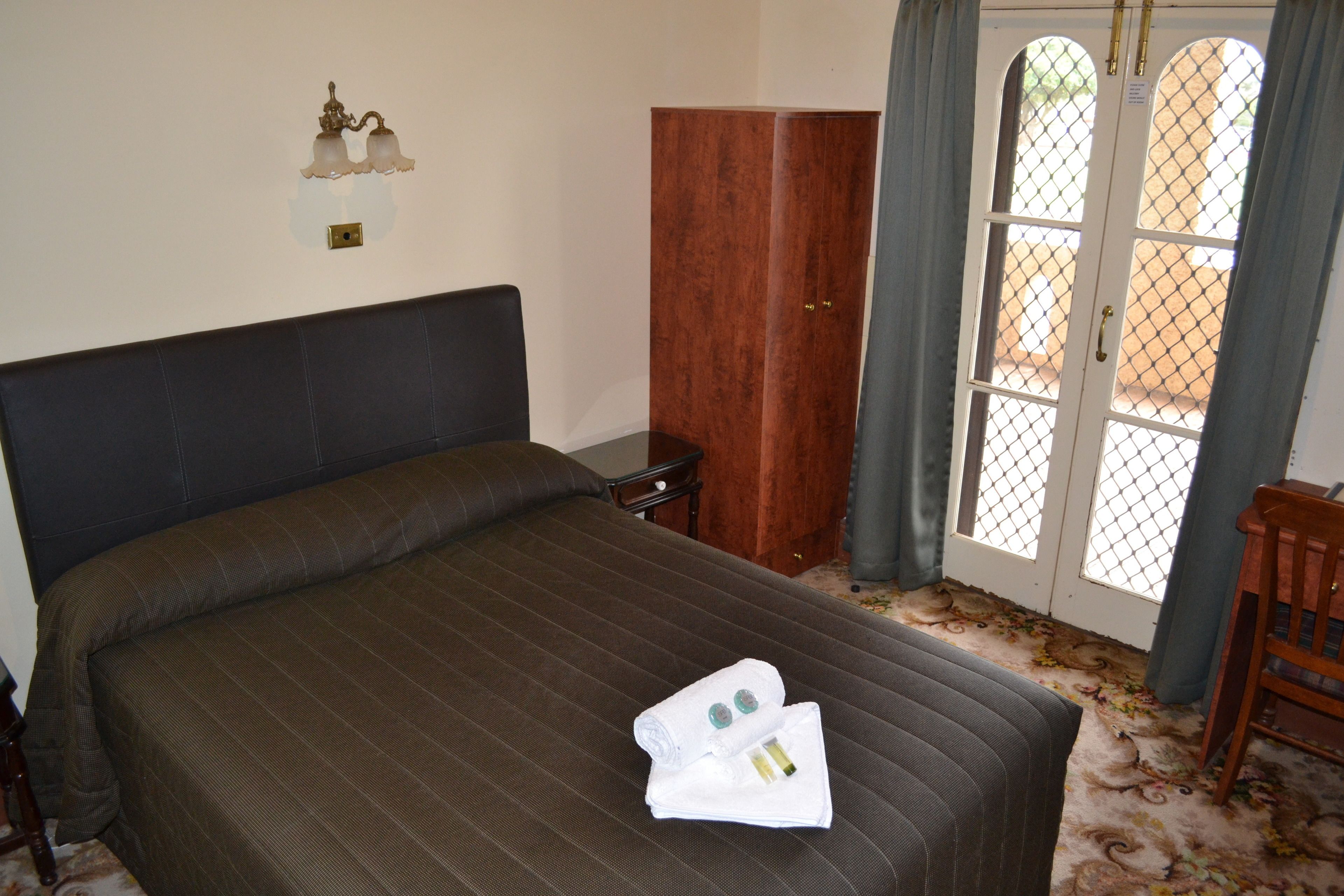 A hotel room with a large bed, a wooden wardrobe, a nightstand, and a window with curtains.