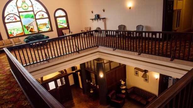A multi-level interior with a wooden railing, a stained glass window, and a seating area with a fireplace. - Hydro Hotel (Leeton)