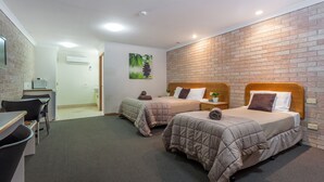Una habitación de hotel con dos camas, un escritorio, sillas y una pared de ladrillo.
