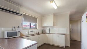Una cocina moderna con armarios blancos, un microondas y un ventanal con persianas.