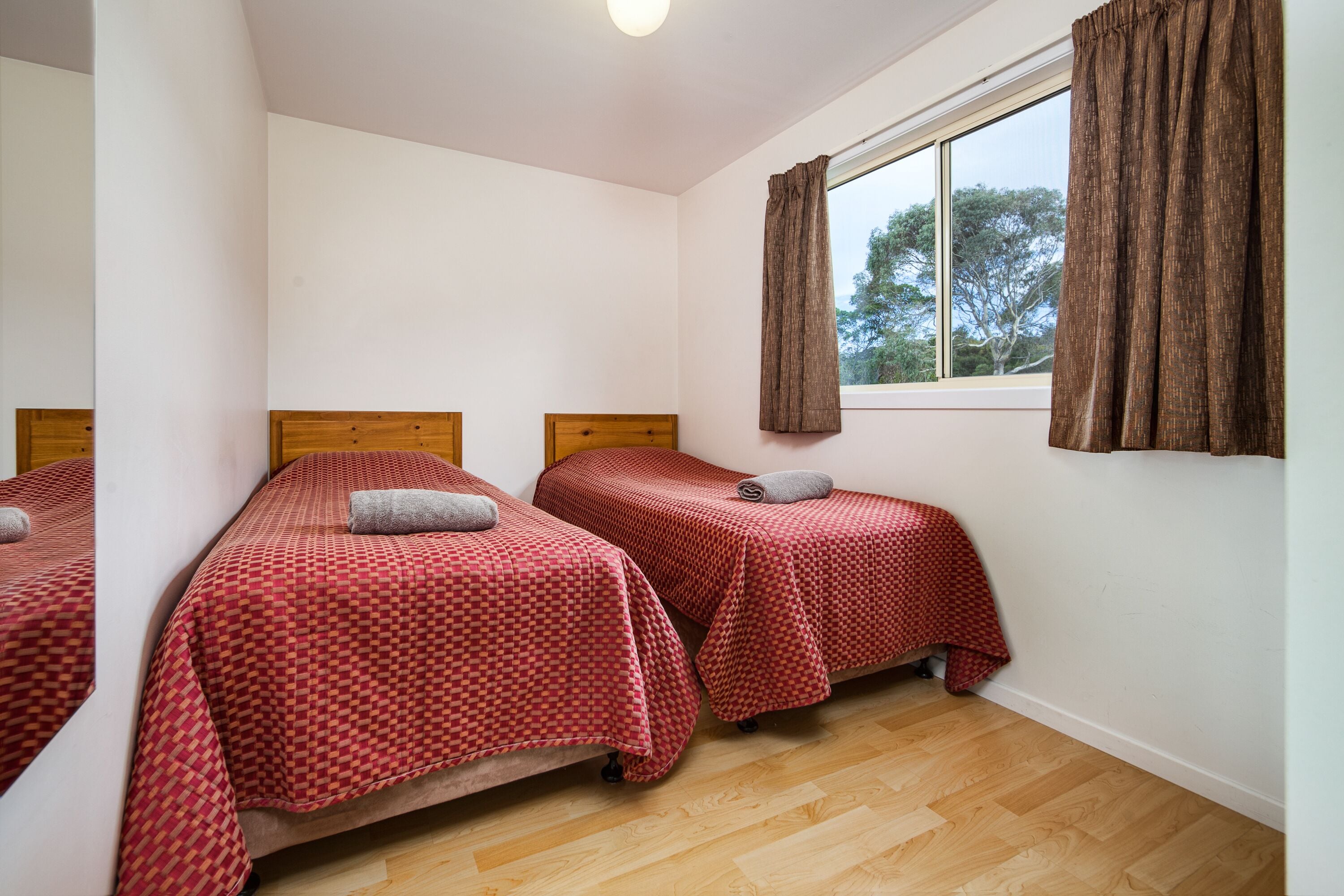 A room with two single beds, wooden headboards, and a window with curtains.