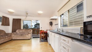 Een moderne keuken met witte kastjes en een zwart aanrecht, een zithoek met een houten tafel en stoelen, en een woonkamer met een beige bank.