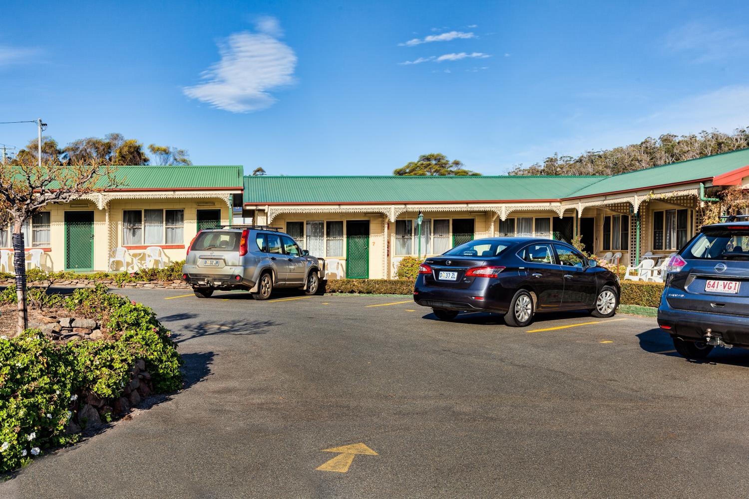 A motel with a green roof, multiple parking spaces, and a clear sky.