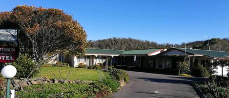 Un motel à deux étages, doté d’un toit végétalisé, entouré de verdure et surplombant un ciel dégagé.