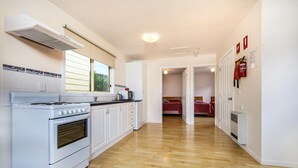 Een keuken met een fornuis, oven en een raam. Een gang leidt naar een slaapkamer met een bed.